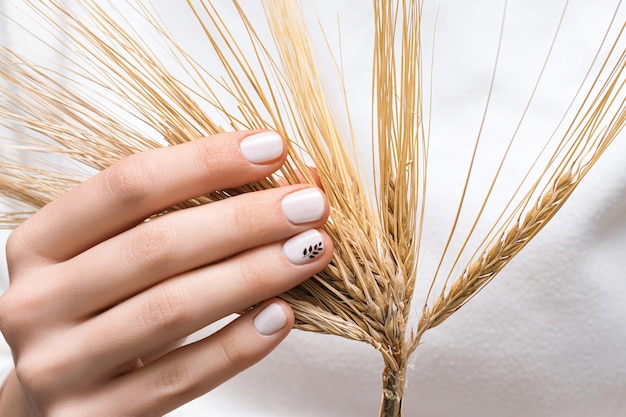 Mano femenina con diseño de uñas blanco, de cerca.