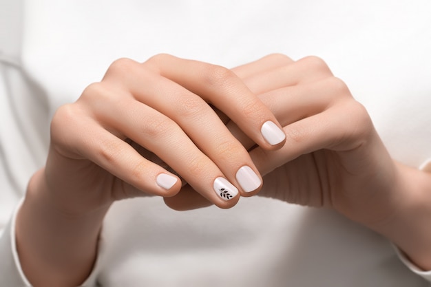 Mano femenina con diseño de uñas blanco, de cerca.