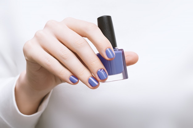 Mano femenina con diseño de uñas púrpura con botella de esmalte de uñas
