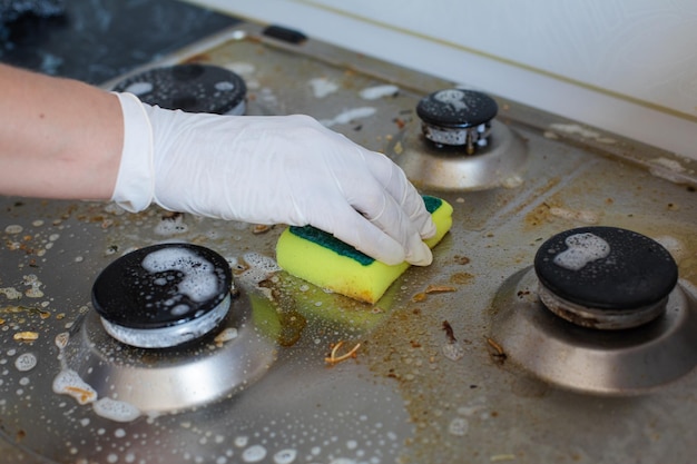 Mano femenina doméstica con guantes limpiando la estufa sucia después de cocinar usando una esponja para lavar Mujer ama de casa disfrutando de la vista superior del primer plano del hogar diario