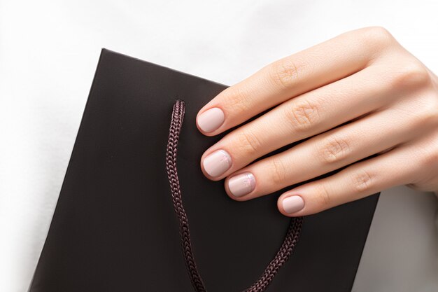 Mano femenina con hermoso diseño de uñas de color beige sostenga bolso elegante oscuro sobre fondo blanco