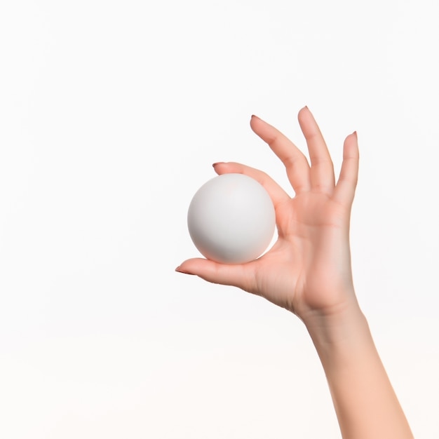 La mano femenina que sostiene la bola de espuma de poliestireno en blanco blanco contra el blanco.