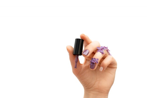 Mano femenina que sostiene la botella púrpura del esmalte de uñas. Concepto de primavera.