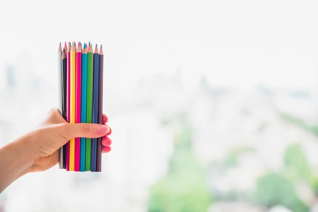 Mano femenina que sostiene el conjunto de lápices de colores contra el fondo borroso