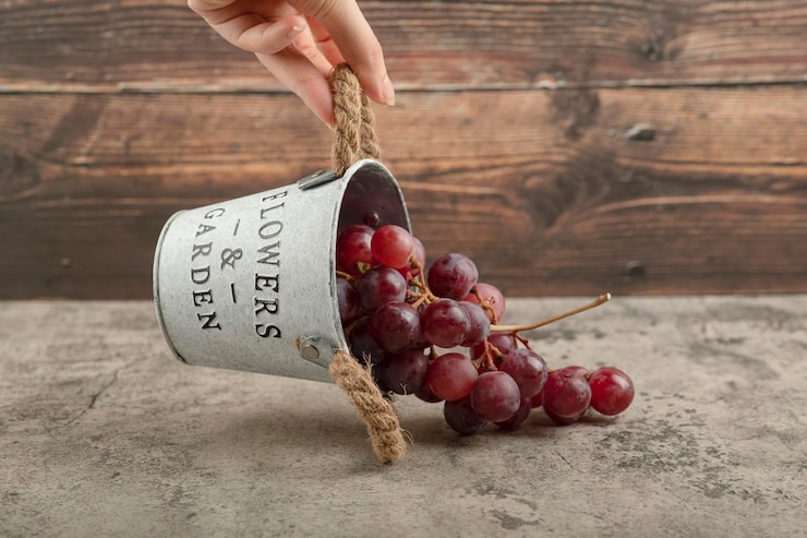 Foto gratuito mano femenina que sostiene el cubo de metal de uvas rojas en la mesa de mármol.