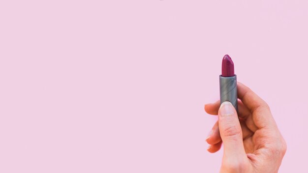 Mano femenina que sostiene el lápiz labial oscuro de la sombra en fondo rosado