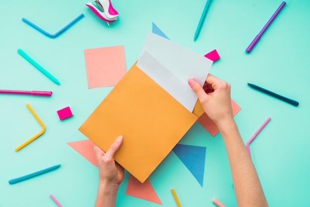 Mano femenina quitando la tarjeta del sobre sobre los accesorios de papelería