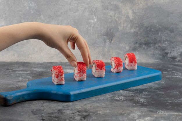 Mano femenina recogiendo rollo de sushi rojo de la tabla de cortar azul