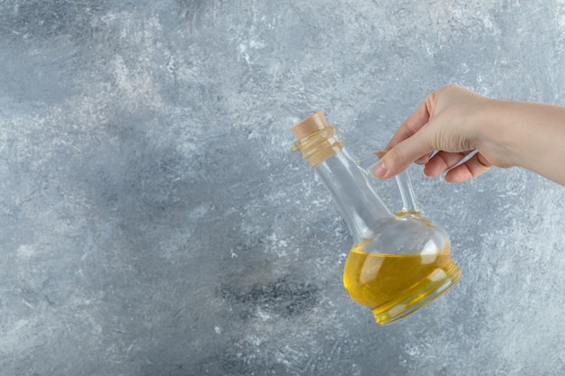 Mano femenina sosteniendo una botella de aceite vegetal sobre fondo gris.