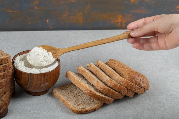 Foto gratuita mano femenina sosteniendo una cuchara de madera de harina y rebanadas de pan.