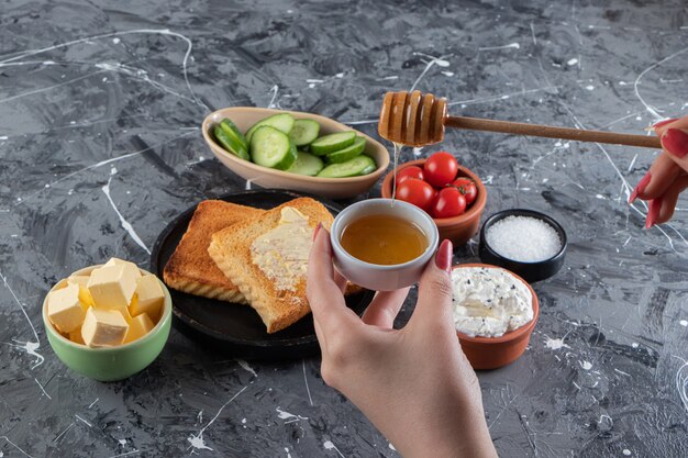 Mano femenina sosteniendo una cuchara de miel en la mesa del desayuno.