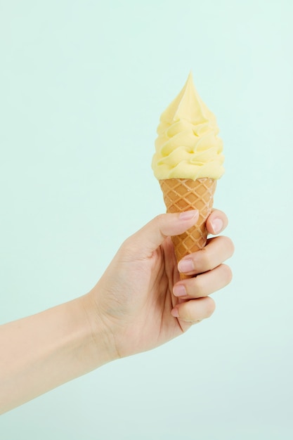 Mano femenina sosteniendo un delicioso helado suave en un cono de galleta crujiente en la pared azul