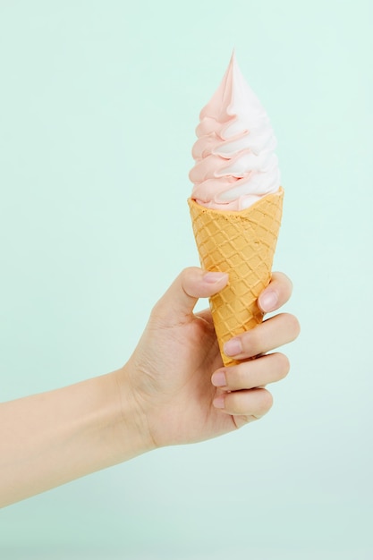 Mano femenina sosteniendo un delicioso helado suave en un cono de galleta crujiente sobre superficie azul