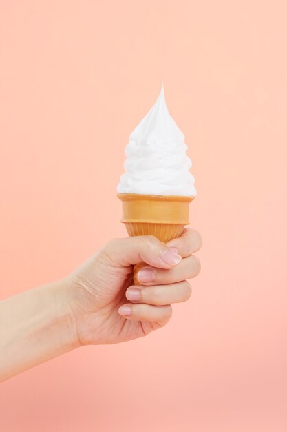 Mano femenina sosteniendo un delicioso helado suave en un cono de waffle crujiente en una escena rosa