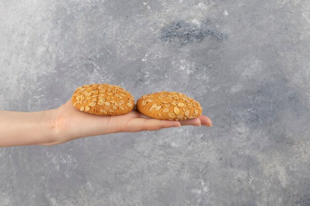 Mano femenina sosteniendo dos galletas de avena en la superficie de mármol