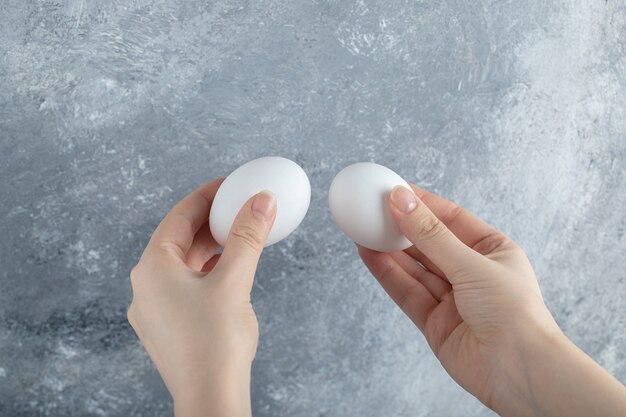 Mano femenina sosteniendo dos huevos en la mesa gris.