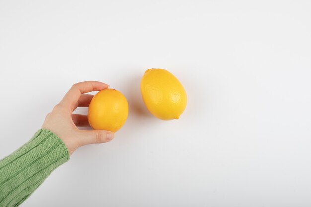 Mano femenina sosteniendo limón amarillo fresco sobre blanco.