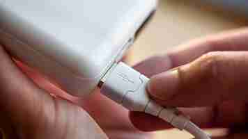 Foto gratuita una mano femenina sostiene un cable usb blanco y un banco de energía blanco, cargando el teléfono con un banco de energía, de cerca.