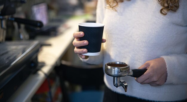 Una mano femenina sostiene un soporte y un vaso el proceso de elaboración del café