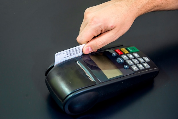 Mano femenina con tarjeta de crédito y terminal de banco, Máquina de tarjeta o pos terminal con tarjeta de crédito blanco en blanco insertado aislado en fondo negro