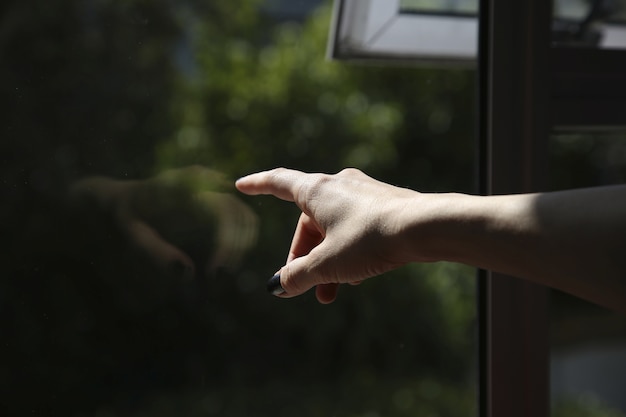 Mano femenina tocando una ventana, apuntando hacia afuera