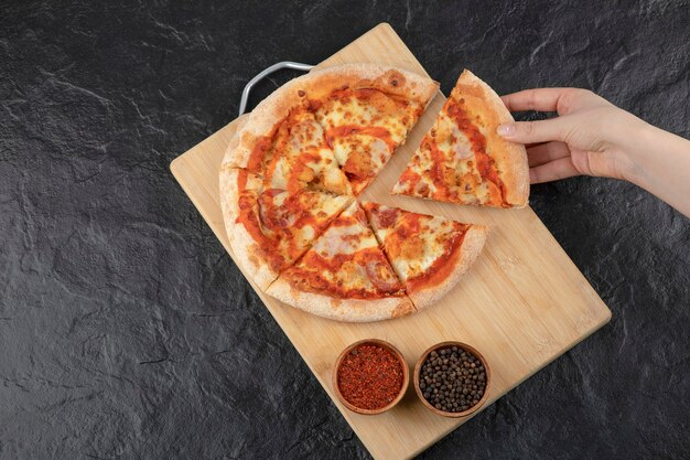 Mano femenina tomando un trozo de pizza de búfalo de tablero de madera.