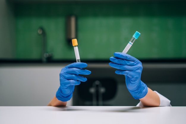 Una mano con guantes de goma sostiene dos tubos de ensayo con el medicamento.