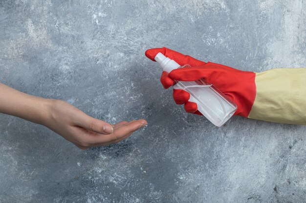 Mano en guantes protectores rociando etanol a mujer.