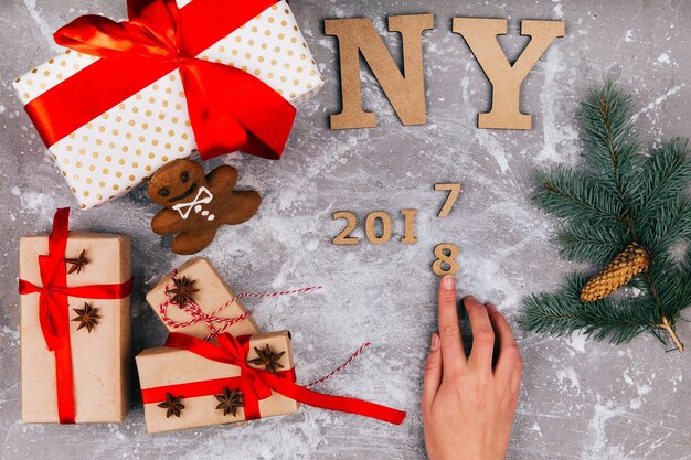 La mano hace el número 2017 a 2018 en el suelo gris cubierto con cajas de regalo de Navidad