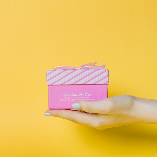 La mano de la hembra que sostiene el rectángulo rosado en fondo amarillo