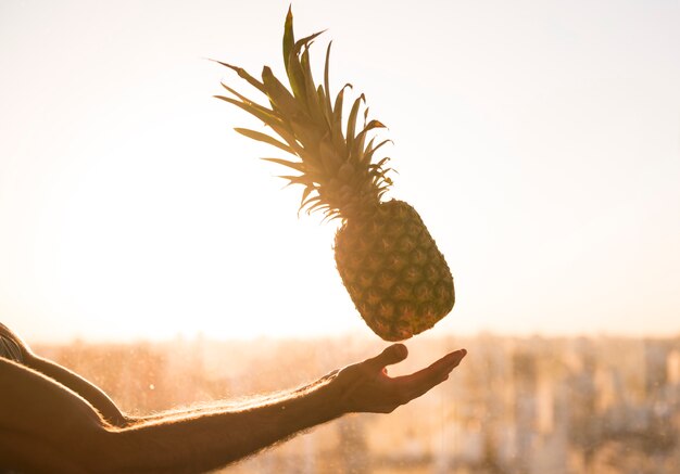 La mano del hombre arrojando la piña en el aire contra la luz solar brillante.