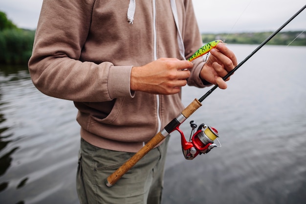 La mano del hombre con cebo y barra de pesca