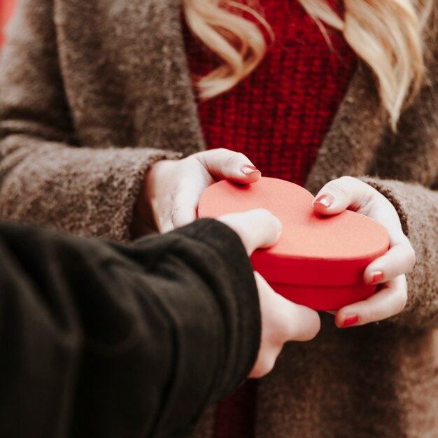 Mano del hombre dando caja de corazón presente para mujer