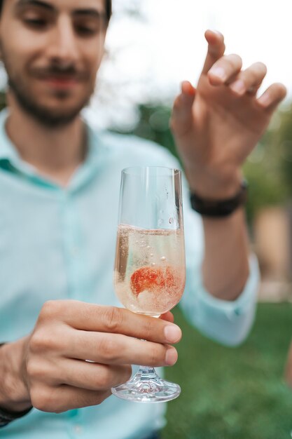 La mano del hombre deja caer una fresa en un vaso con vino espumoso. Hermosa vida, celebración