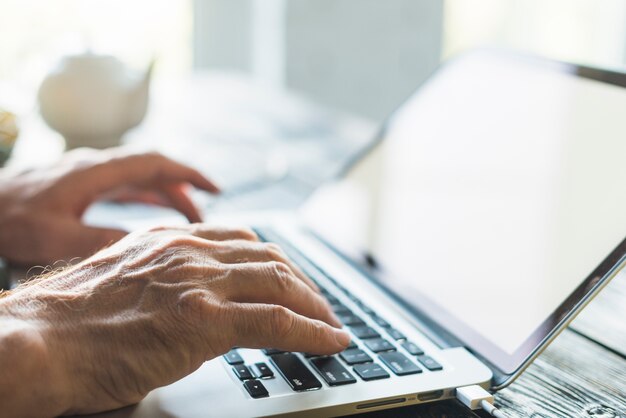 La mano del hombre escribiendo en la computadora portátil sobre el escritorio de madera