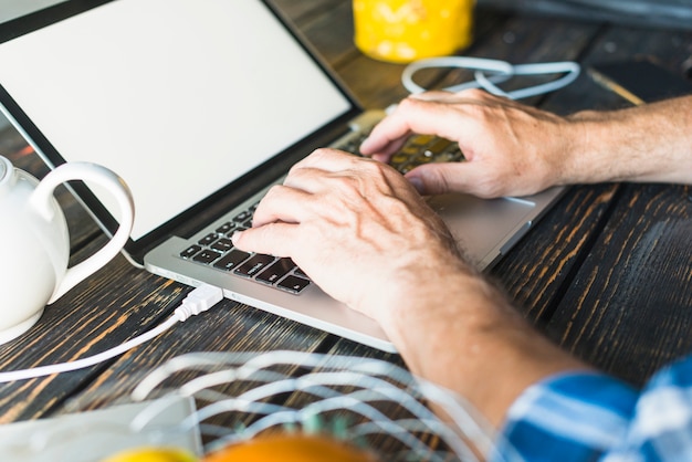 La mano del hombre escribiendo en la computadora portátil sobre el escritorio de madera