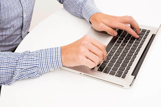 La mano del hombre escribiendo en la computadora portátil sobre la mesa blanca
