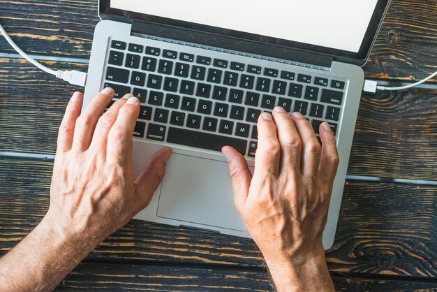 La mano del hombre escribiendo en el teclado de la computadora portátil sobre el escritorio de madera