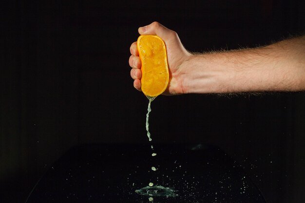 La mano de hombre fuerte aprieta la mitad de una naranja sobre la mesa de vidrio