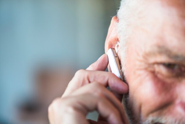 La mano del hombre mayor que pone el receptor de cabeza del bluetooth en su oído