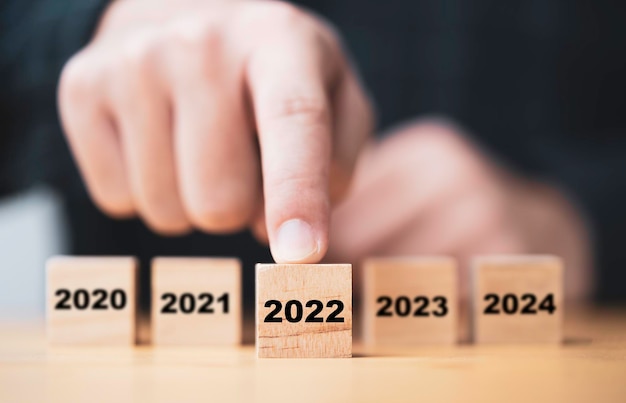 Mano de hombre de negocios empujando el año 2022 que imprime la pantalla en un bloque de cubo de madera para la preparación del año nuevo y comienza un nuevo concepto de negocio.