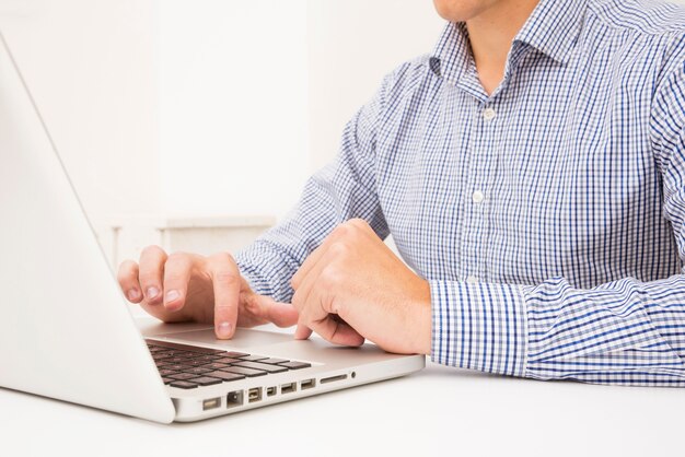 Mano del hombre de negocios de navegación en la computadora portátil sobre la mesa blanca