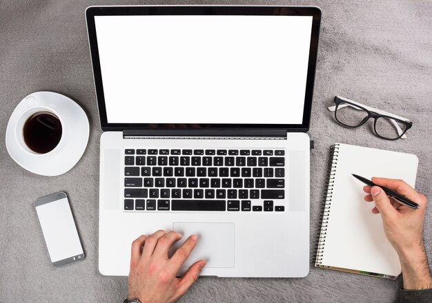 Mano de un hombre de negocios usando tableta digital escribiendo en una libreta espiral sobre el escritorio gris