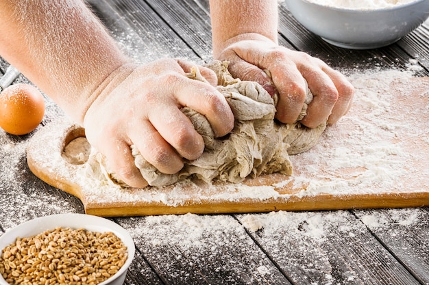 Mano del hombre preparando masa y granos de trigo en el cuenco sobre la mesa