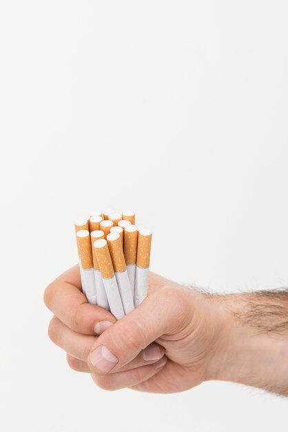 La mano de un hombre que sostiene el montón de cigarrillos aislados en el contexto blanco