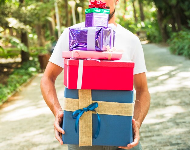 La mano del hombre que sostiene la pila de regalos multicolores