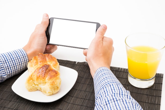 La mano del hombre que sostiene el teléfono celular con pantalla en blanco en blanco a la hora del desayuno