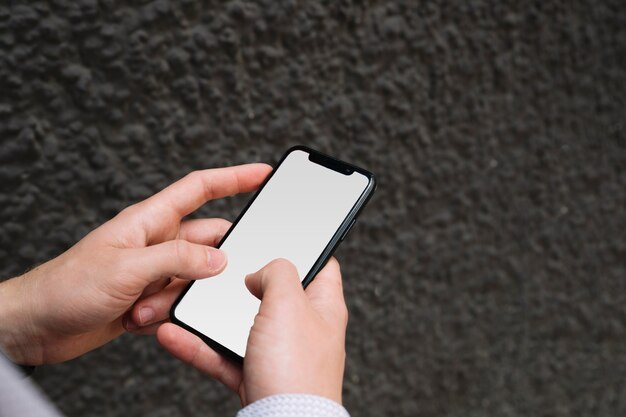 Mano del hombre que sostiene el teléfono celular con pantalla en blanco