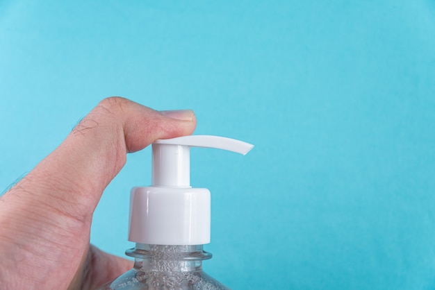 Mano del hombre en un recipiente con gel de alcohol en la luz azul