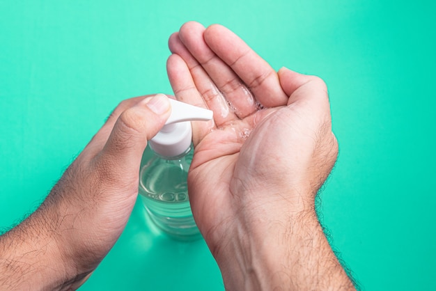 Mano del hombre en un recipiente con gel de alcohol en la luz azul